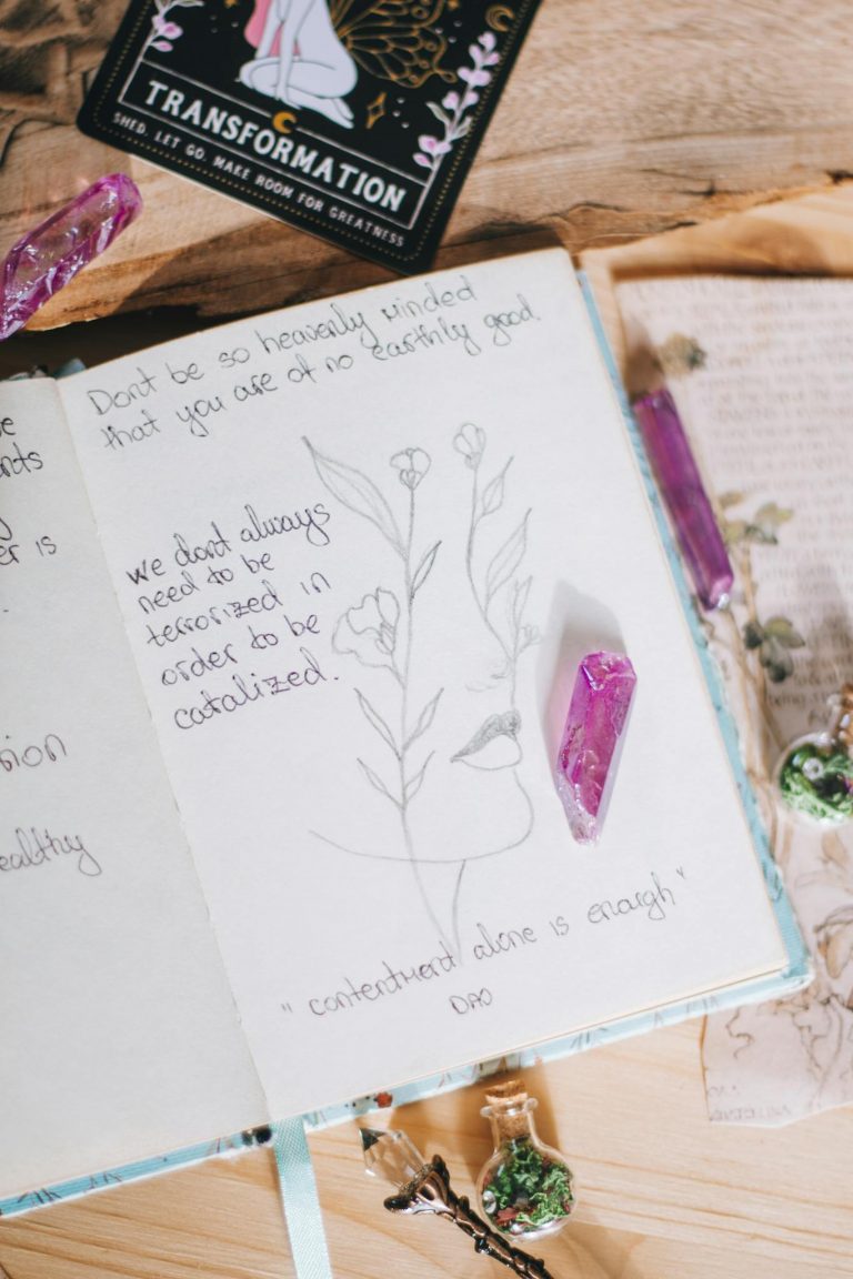 Open journal with esoteric writings, adorned with pink crystals and delicate sketches.